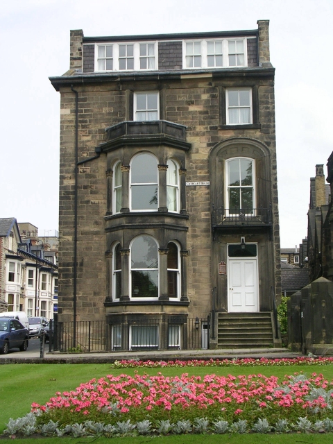 Cathcart House on the corner of Raglan Street, Harrogate: a three-storey honey-stone Victorian townhouse with a bay window, balustrade and dormer, the same Yorkshire-stone construction as Raglan Chambers two doors down.